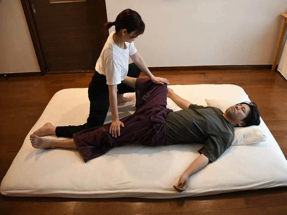 床に敷いたマットの上で、服を着たままの利用者の脚をセラピストが伸ばすタイ古式マッサージの全景