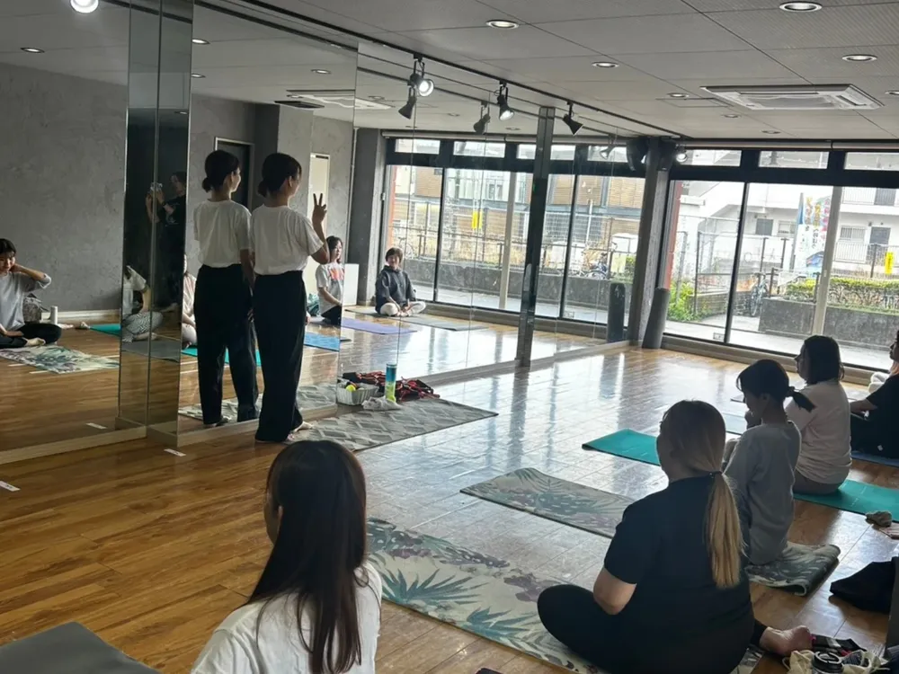 あきる野市のヨガスタジオで開いたコラボレッスンの風景。鏡張りのスタジオで、マットに座った参加者と、前に立つ2名